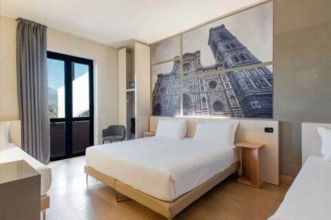 Room interior at B&B Hotel Firenze Nuovo Palazzo di Giustizia featuring two beds, wooden floors, wardrobe, chair, and large window with curtain