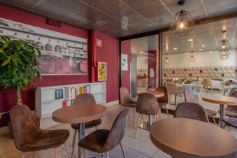 Interior seating area at B&B Hotel Firenze Nuovo Palazzo di Giustizia with round tables, brown chairs, bookshelf, and wall art of a bridge