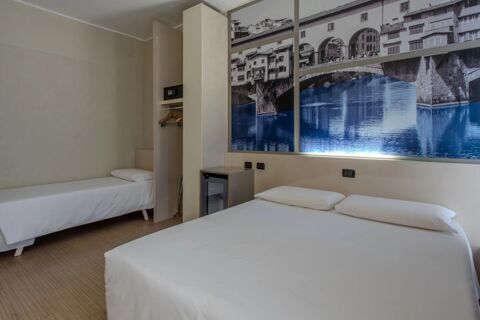 Room at B&B Hotel Firenze Nuovo Palazzo di Giustizia with two twin beds, simple wardrobe with safe, minibar, and wall art of a bridge and river
