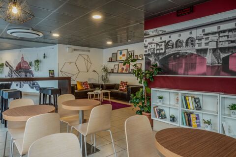 Interior seating area of B&B Hotel Firenze Nuovo Palazzo di Giustizia with wooden tables, chairs, black sofas, and large wall art murals