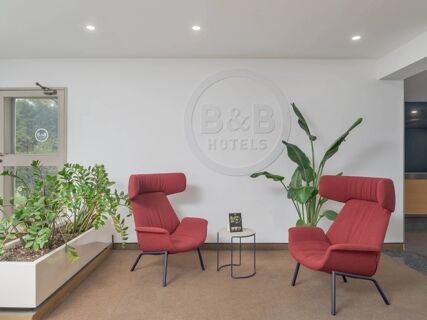 Two red armchairs face each other beside a small round table and plants in the lobby of B&B Hotel Calenzano First