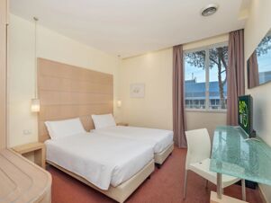 Two single beds with white bedding, a glass desk, television, chair, window with curtains, and wall lamps in B&B Hotel Calenzano First room
