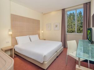 Room at B&B Hotel Calenzano First with a double bed, bedside tables, pendant lights, window with curtains, and a TV on a glass table