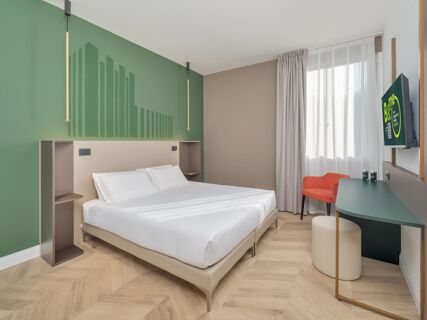 Modern hotel room at B&B Hotel Calenzano First with a double bed, green and beige walls, desk, TV, and orange chair