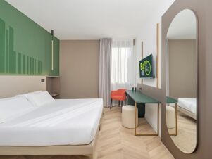 Modern hotel room at B&B Hotel Calenzano First with white bed linen, green accent wall, orange chair, and wall-mounted TV