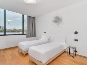 Two single beds with white linens, a small round glass side table, and large window in a B&B Hotel Alba room