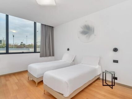 Two single beds with white linens, a small round glass side table, and large window in a B&B Hotel Alba room