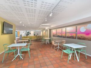 Dining area with white tables, green and beige chairs, terracotta floor tiles, and colorful wall art at B&B Hotel Alba