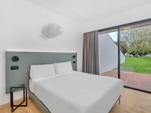 Double bed with white linens in a clean room at B&B Hotel Alba featuring a green headboard, small glass table, and sliding glass doors