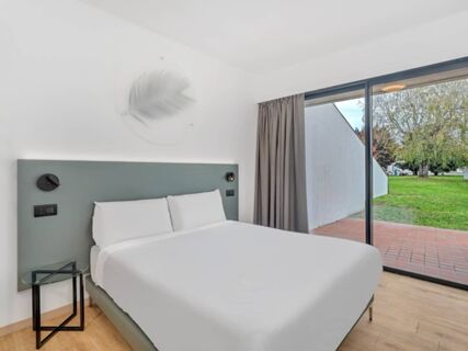 Double bed with white linens in a clean room at B&B Hotel Alba featuring a green headboard, small glass table, and sliding glass doors