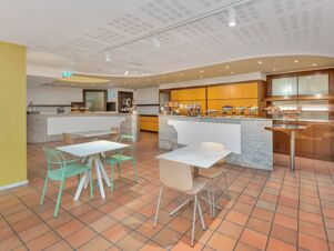 Bright breakfast area at B&B Hotel Alba with tables, chairs, buffet counters, fruit bowls, and baked goods displays