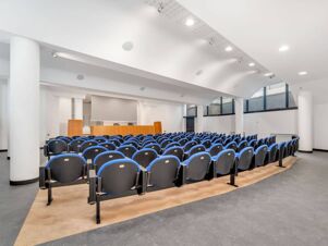 Empty conference room at B&B Hotel Alba with rows of blue and black chairs facing a wooden podium and screen