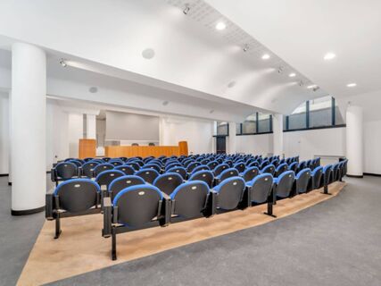Empty conference room at B&B Hotel Alba with rows of blue and black chairs facing a wooden podium and screen