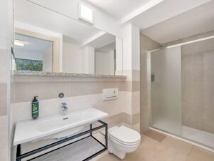 Modern bathroom at B&B Hotel Alba with white sink, wall-mounted toilet, large mirror, and glass shower enclosure