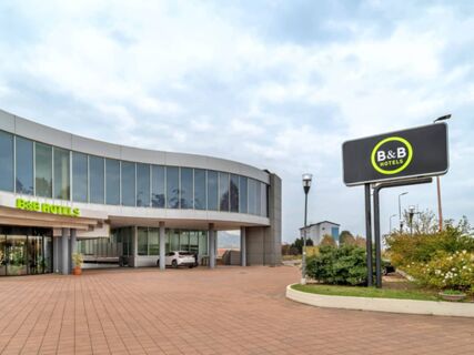 Modern curved glass building with a B&B Hotels sign and a car parked near the entrance of B&B Hotel Alba