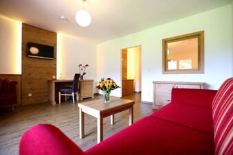 Helles Wohnzimmer mit rotem Sofa, Holzm&ouml;beln und Blumen auf dem Tisch im Hotel-Restaurant-Cafe Friedenseiche pr&auml;sentiert ein gem&uuml;tliches Ambiente.