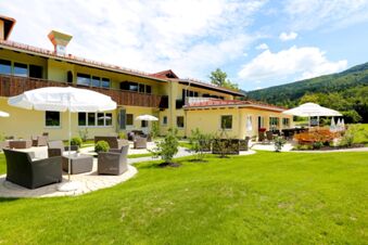 Sonnige Gartenansicht mit Sitzgruppen und Sonnenschirmen vor dem Hotel-Restaurant-Cafe Friedenseiche in gr&uuml;ner Landschaft und blauem Himmel.