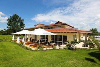 Au&szlig;enansicht mit Terrasse und Sonnenschirmen des Hotel-Restaurant-Cafe Friedenseiche bei sonnigem Wetter und gr&uuml;ner Umgebung.