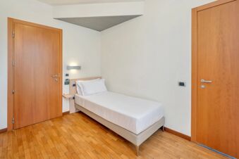 Single bed with white linens next to wooden doors and wall-mounted light in a room at B&B HotelPark Hotel Mondov&igrave;