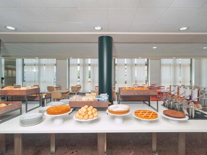 A breakfast buffet with various types of bread, pastries, cakes, and chairs in a dining area at B&B HotelPark Hotel Mondov&igrave;