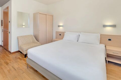 Bedroom at B&B HotelPark Hotel Mondov&igrave; featuring a large bed with white linens, beige armchair, wardrobe, and wall lights