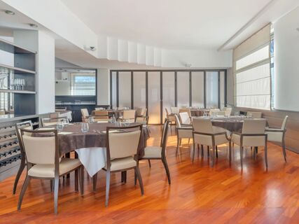 Dining area in B&B HotelPark Hotel Mondov&igrave; with round tables covered in brown and white tablecloths and beige chairs on wooden floor