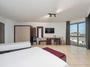 Two beds, wardrobe, wall-mounted TV, desk with chair, window with curtains, and bench in a B&B HotelPark Hotel Mondov&igrave; room
