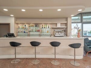 Bar area with four black bar stools, shelves with various bottles and glasses, and a coffee machine at B&B HotelPark Hotel Mondov&igrave;
