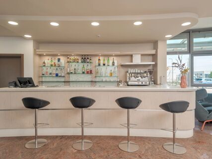 Bar area with four black bar stools, shelves with various bottles and glasses, and a coffee machine at B&B HotelPark Hotel Mondov&igrave;