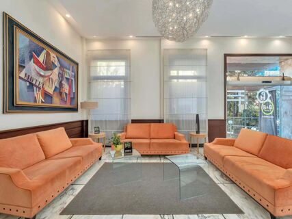 Orange couches surround a gray carpet and glass table in a lobby with modern artwork and lighting at B&B HotelPark Hotel Mondov&igrave;