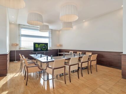 Meeting room with beige chairs around a U-shaped table, a TV screen, floor lamps, and hanging lights at B&B HotelPark Hotel Mondov&igrave;