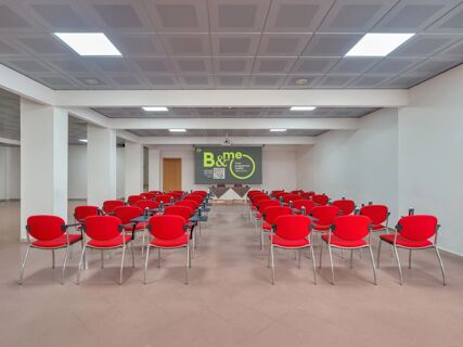 Conference room with rows of red chairs facing a projector screen in a modern meeting space at B&B HotelPark Hotel Mondov&igrave;