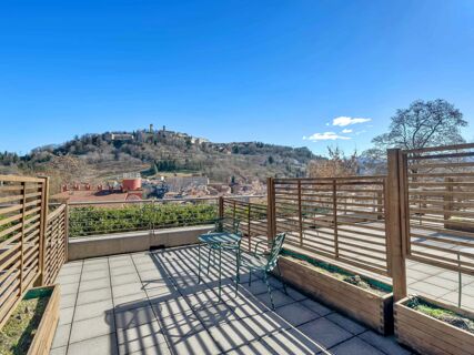 Outdoor tiled balcony with metal chairs and table, wooden fencing, and a view of a hillside town at B&B HotelPark Hotel Mondov&igrave;