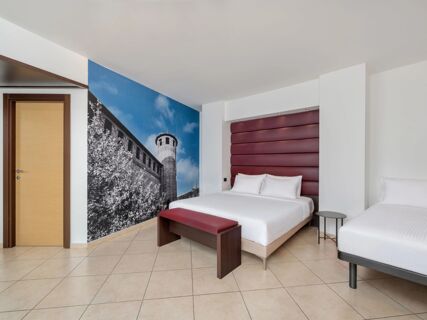 Room at B&B HotelPark Hotel Mondov&igrave; with two beds, burgundy padded headboard, bench, side table, and mural of a tower on the wall