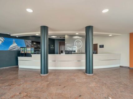 Reception area with light-colored counter, two black pillars, drinks fridge, and B&B HotelPark Hotel Mondov&igrave; logo on glass panel