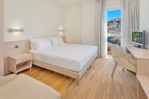 A clean hotel room at B&B HotelPark Hotel Mondov&igrave; featuring a neatly made double bed, wooden nightstand, desk, chair, and window with view outside