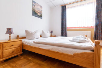 A simple wooden bed with white linens and pillows in a bright room at Hotel am Gothensee with two bedside tables and lamps