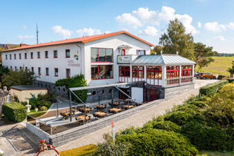 Hotel am Gothensee with outdoor seating area, glass-covered terrace, white facade, and surrounding greenery on a sunny day