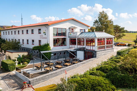Hotel am Gothensee with outdoor seating area, glass-covered terrace, white facade, and surrounding greenery on a sunny day