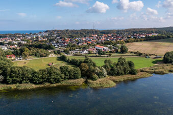 Aerial view of a lakeside town with houses, fields, trees, and a visible building identified as Hotel am Gothensee in the distance