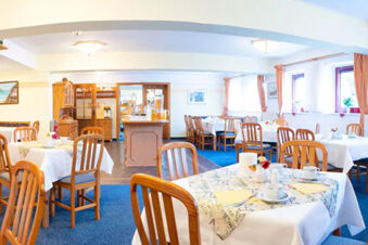 Dining area of Hotel am Gothensee with wooden chairs, white tablecloths, and beverage dispensers on a central island