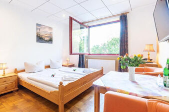 Bright hotel room at Hotel am Gothensee with a wooden double bed, nightstands, lamps, a table with flowers, and an open window