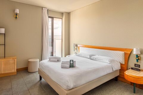 A neatly made double bed with white linens and towels in a room at B&B Hotel Chioggia Airone with a balcony door and patterned walls