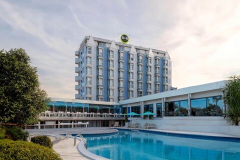 B&B Hotel Chioggia Airone with a large outdoor swimming pool, blue and white building, green trees, and seating area with umbrellas