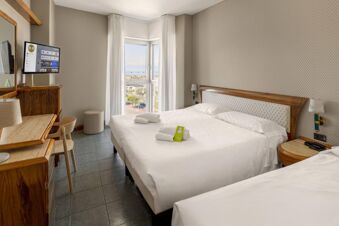 Double room at B&B Hotel Chioggia Airone with two beds, a TV, desk, chair, window, and view outside the building