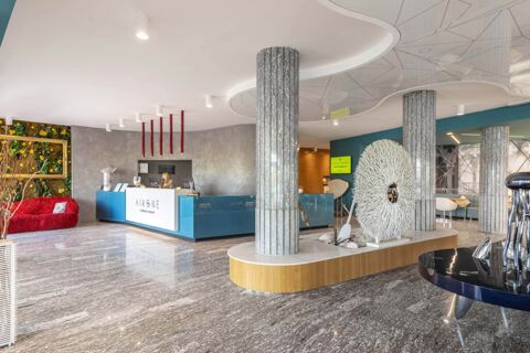 Modern hotel lobby with marble flooring, grey pillars, blue reception desk, red sofa, and decorative art at B&B Hotel Chioggia Airone