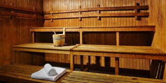 Wooden interior of a sauna with tiered benches, a wooden bucket with a ladle, and folded towels at Hotel Indigo Rome-St.George