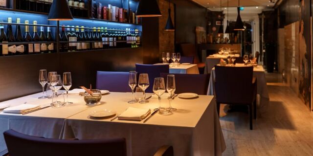 Dining tables with white tablecloths, glassware, plates, and wine bottles on shelves at Hotel Indigo Rome-St.George