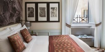 Bed with white linens and patterned pillows and runner, framed black and white photos, and window seating at Hotel Indigo Rome-St.George