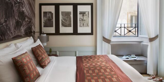 Bed with white linens and patterned pillows and runner, framed black and white photos, and window seating at Hotel Indigo Rome-St.George